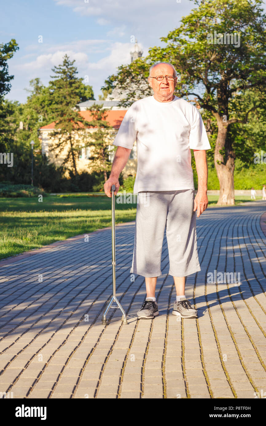 Smiling pensioner enjoying walk in park with stick Stock Photo