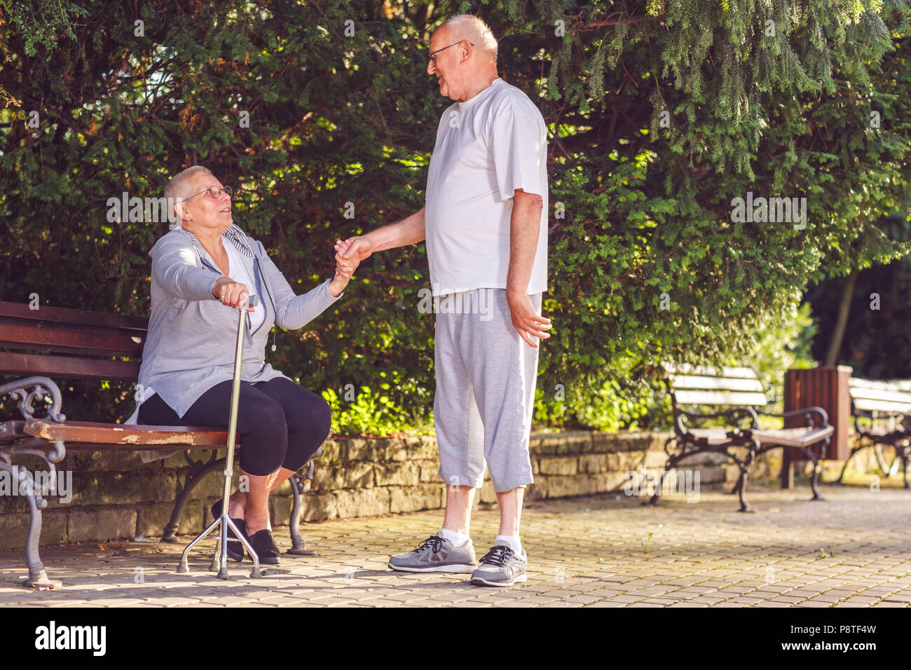 Smiling aging senior man supporting ill wife in the park Stock Photo