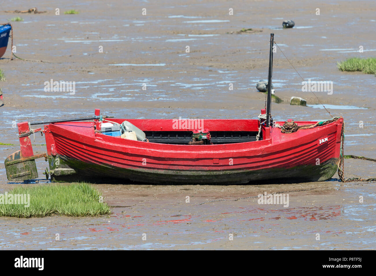 A small red In-shore fishing boat aground and waiting for the tide in Morecambe Bay Stock Photo