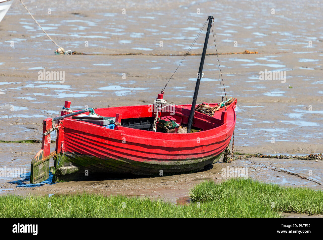 A small red In-shore fishing boat aground and waiting for the tide in Morecambe Bay Stock Photo