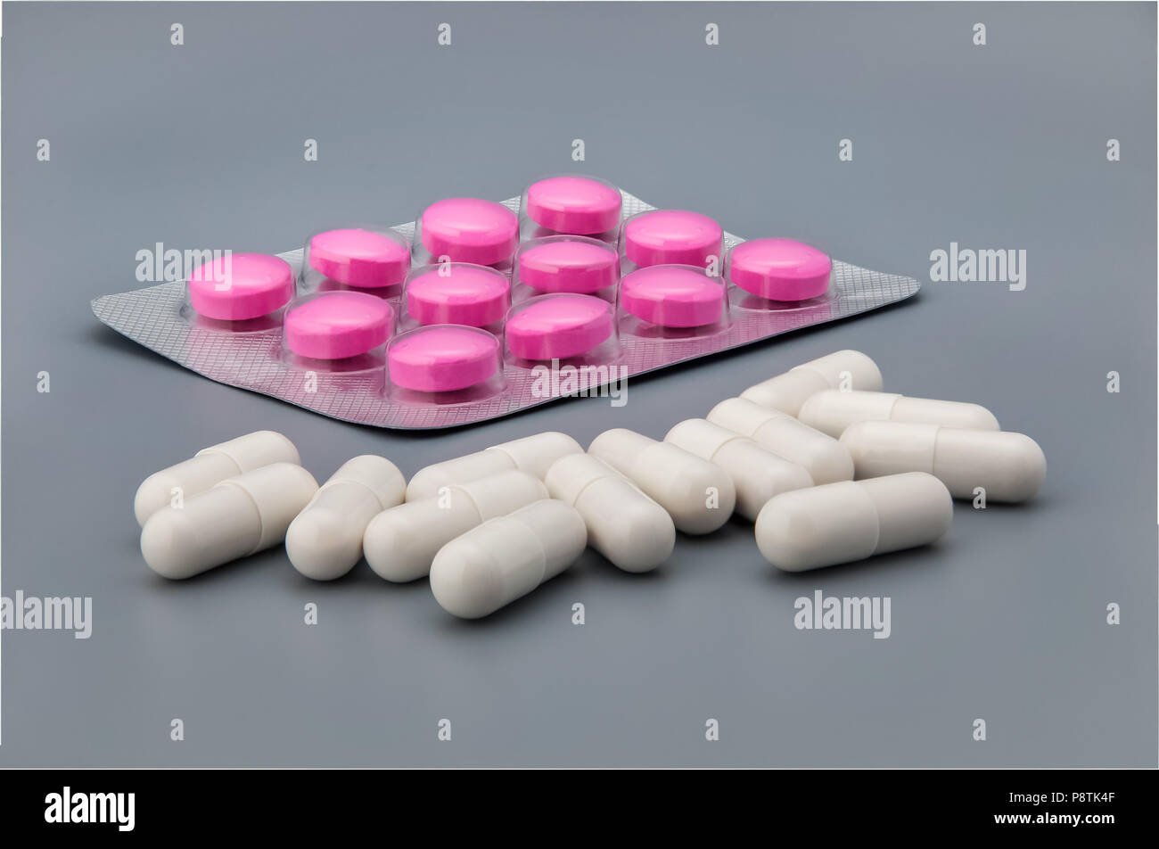 Blister with red tablets and scattered white pills on a gray background. Stock Photo