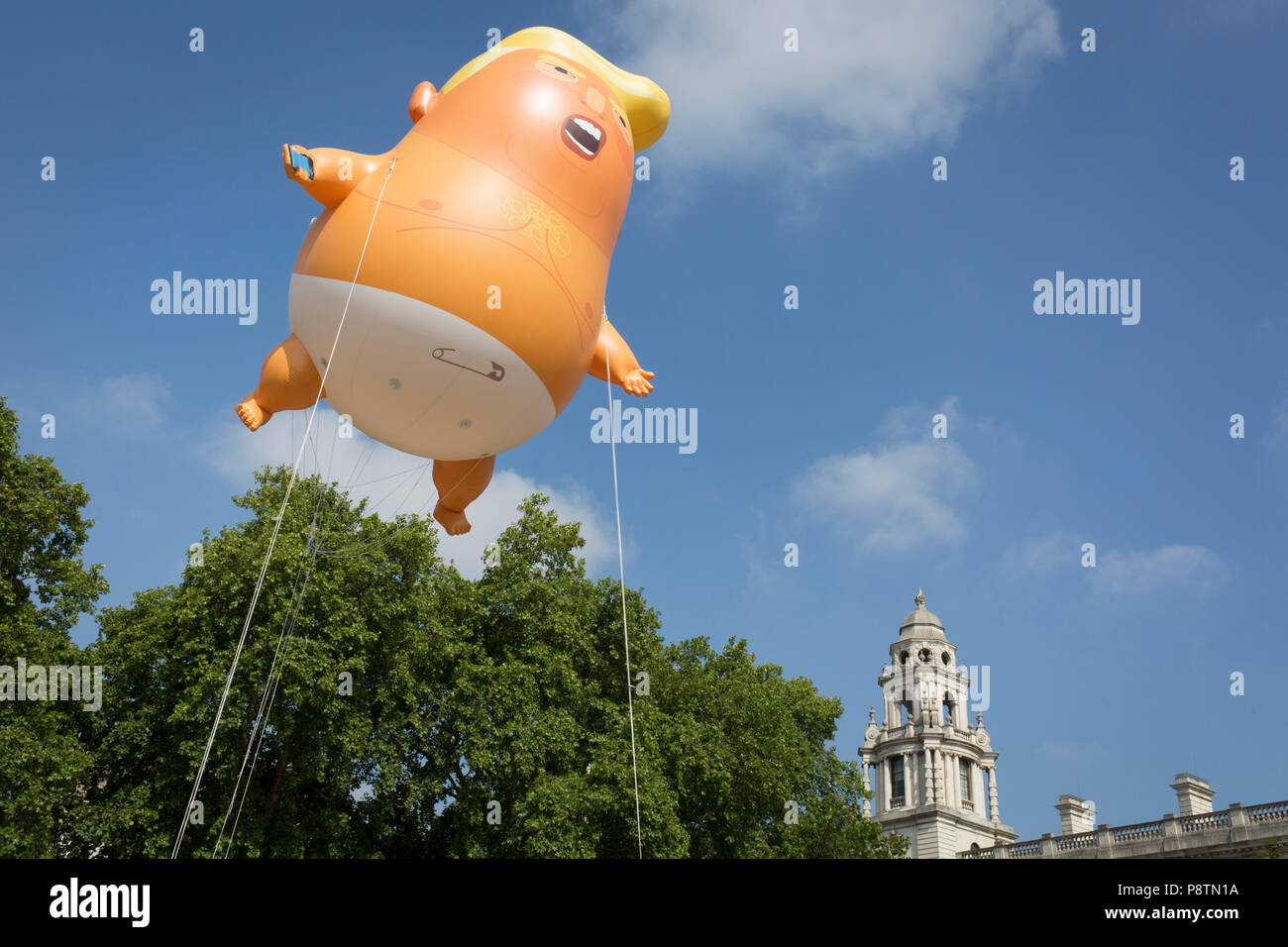 London, UK. 13th July, 2018. The inflatable balloon called Baby Trump flies above Parliament Square in Westminster, the seat of the UK Parliament, during the US President's visit to the UK. Baby Trump is a 20ft high orange blimp depicting the US President as an enraged, smartphone-clutching infant - and given special permission to appear above the capital by London Mayor Sadiq Khan because of its protest rather than artistic nature. It is the brainchild of Graphic designer Matt Bonner. Credit: RichardBaker/Alamy Live News Stock Photo