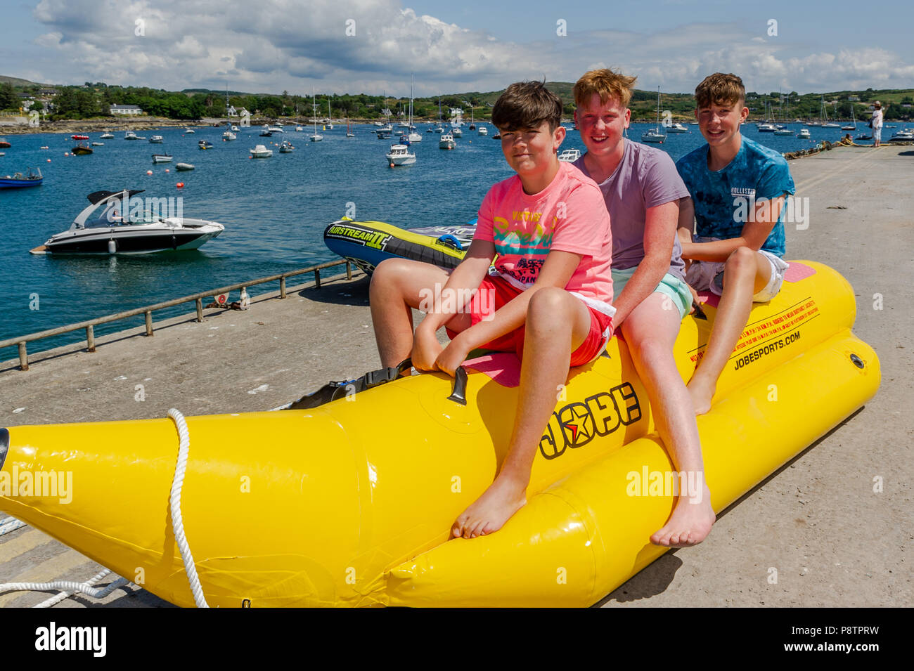 Schull, West Cork, Ireland. 13th July, 2018. Making the most of the hot weather and sitting astride a towable inflatable preparing to have some fun in the water in Schull Harbour are Jamie Donnelly, Tom Casey and Jeremy Kingston, all from Cork city. The rest of the day will have highs of 20° Celsius but the rest of the weekend will be cooler with rain forecast for Sunday. Credit: Andy Gibson/Alamy Live News. Stock Photo