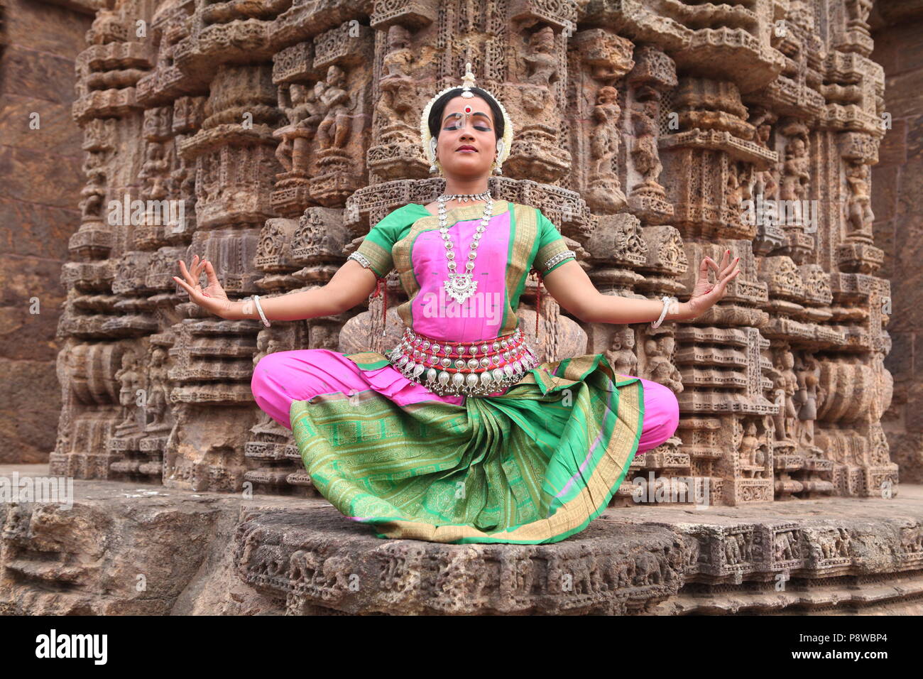 odissi is one of the eight classical dance forms of india,from the state of odisha.here the dancer poses before temples with sculptures Stock Photo