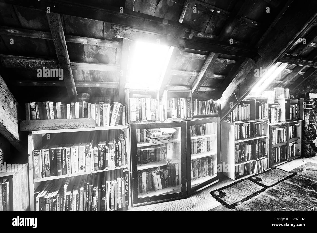 Farm house interior, Farm house interior, attic room reading corner under sunlit roof window, clutter of books on shelves (mono) Stock Photo