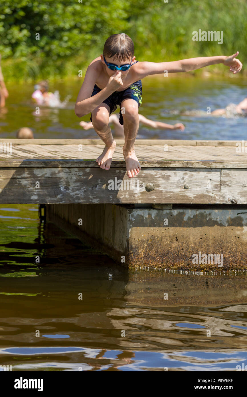 Young boy jumping into lake water from Jetty Stock Photo