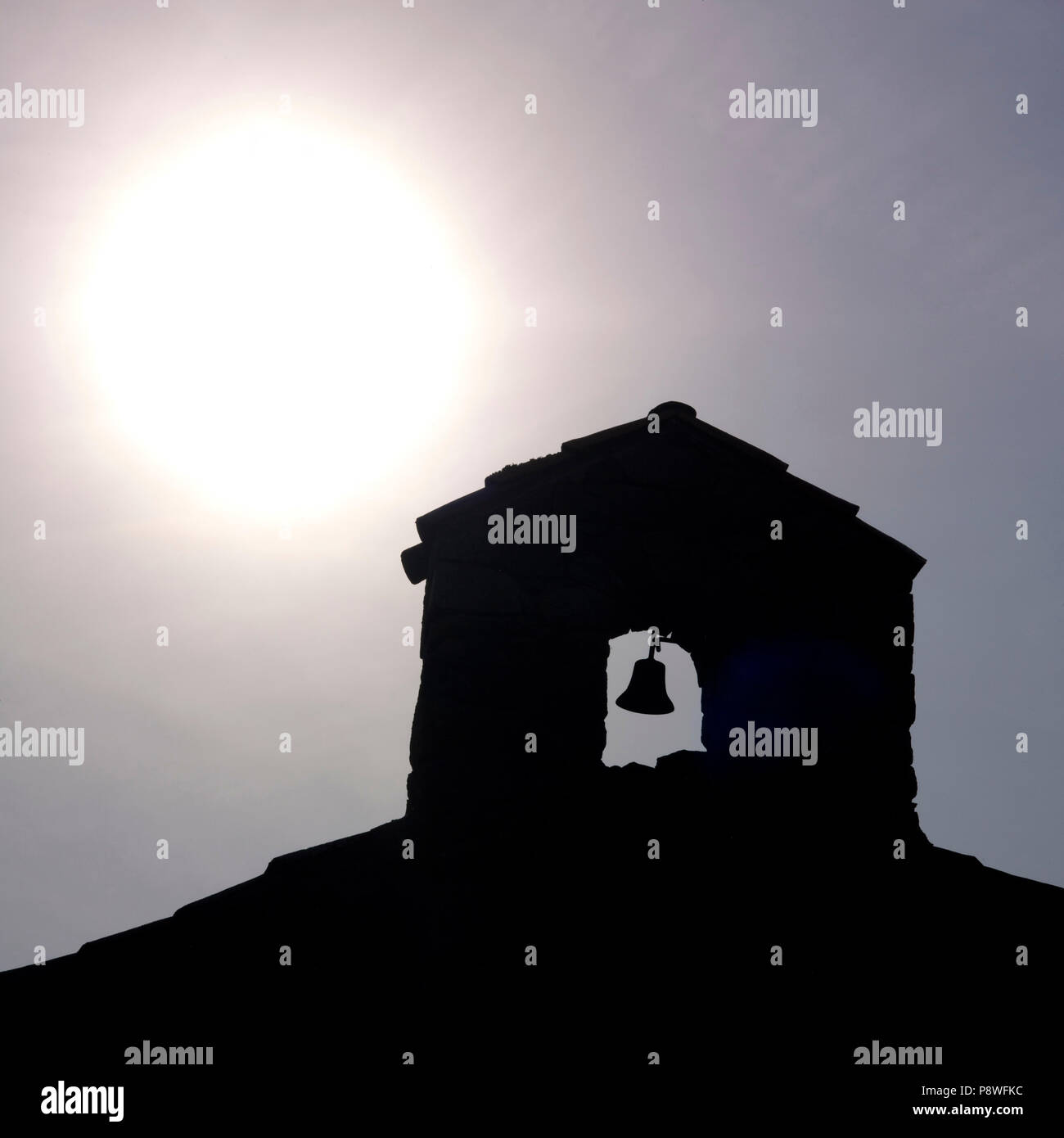Close up of the bell and the bell tower of a small chapel in backlighting, Auvergne, France Stock Photo