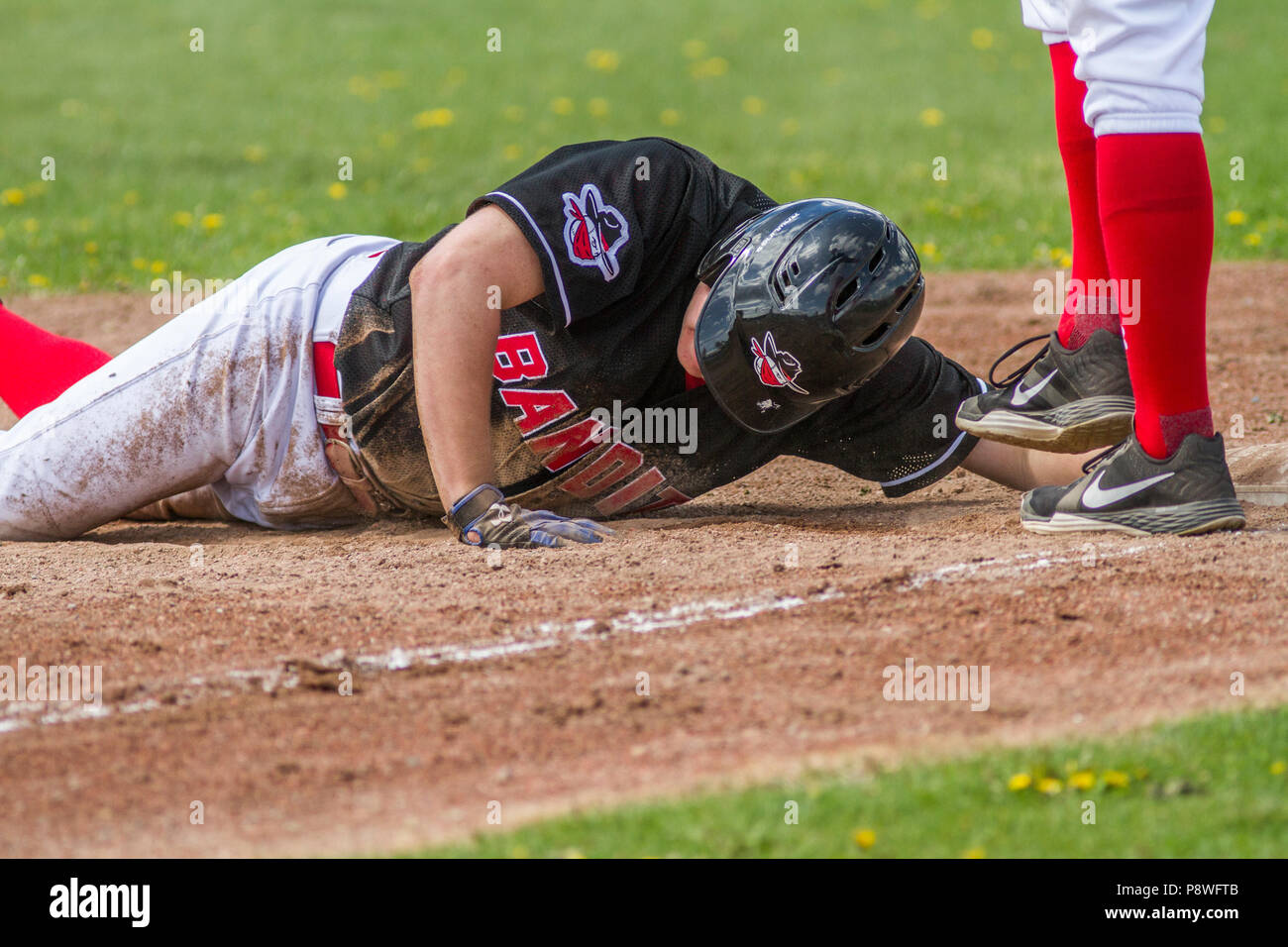 Baseball player sliding , head first, into third base,  boys afternoon junior baseball game. Cranbrook, BC. Stock Photo