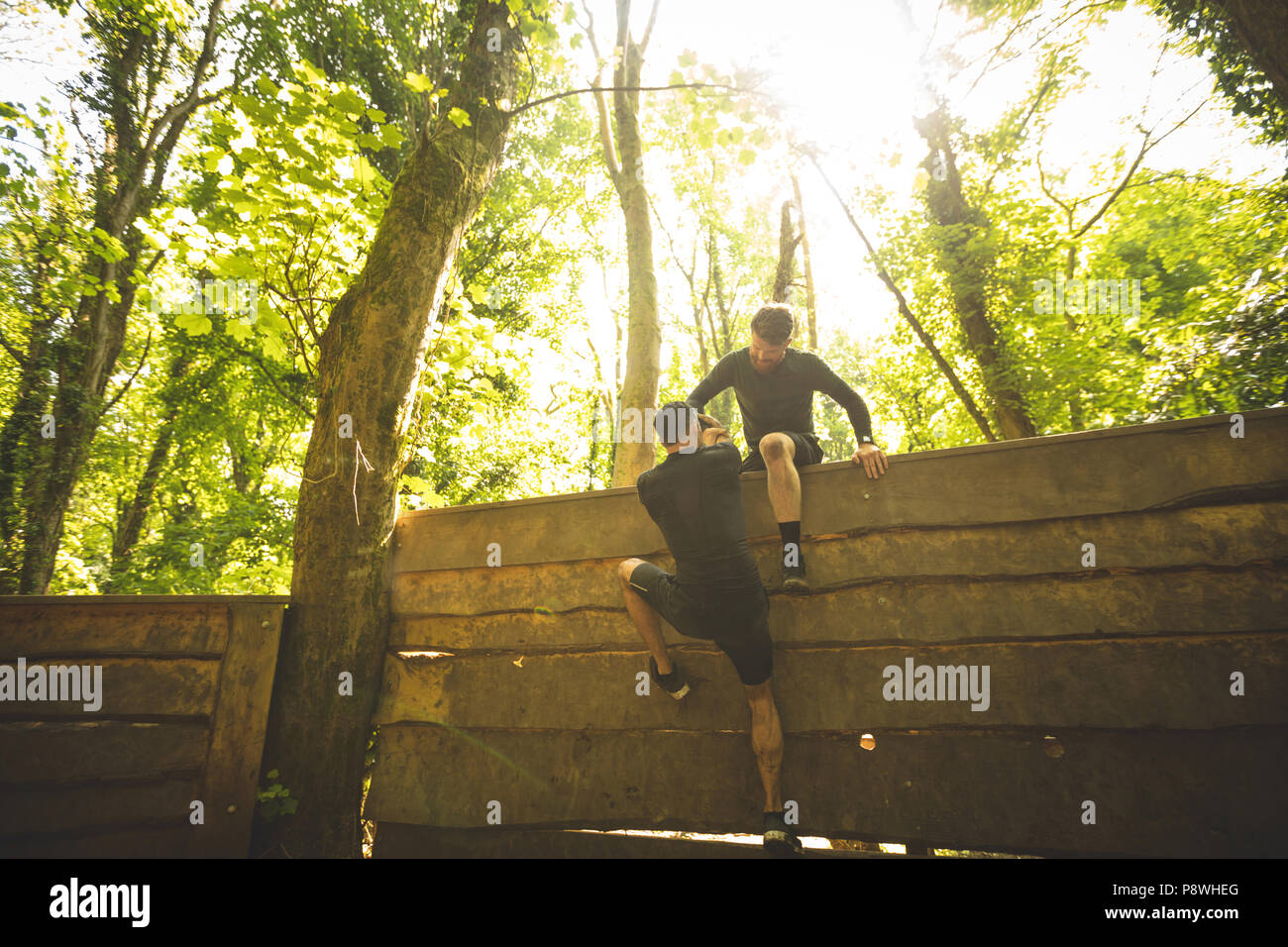 Fit man assisting his teammate to climb a wooden wall Stock Photo