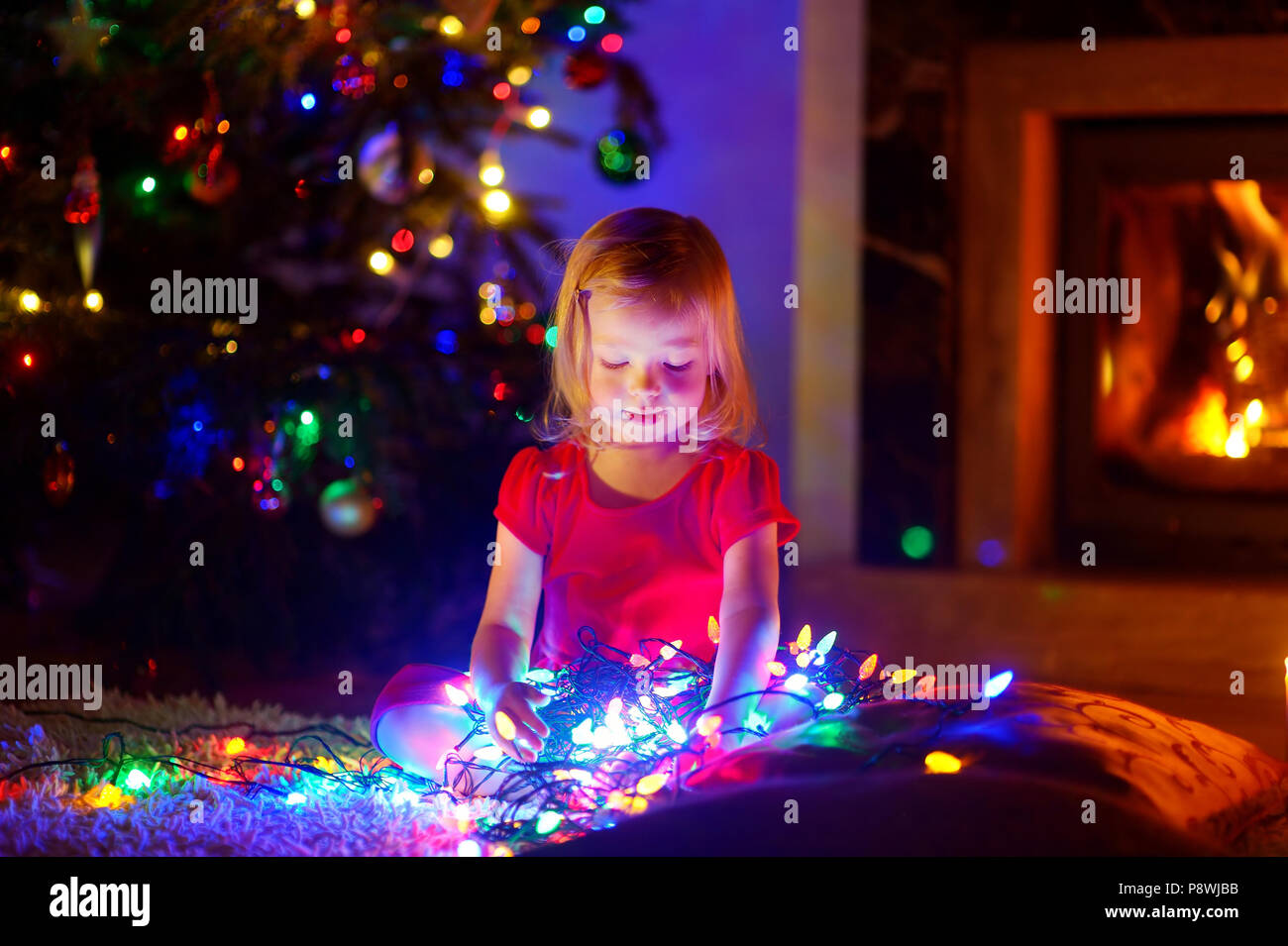 Adorable Little Girl Playing With Christmas Lights By A Fireplace