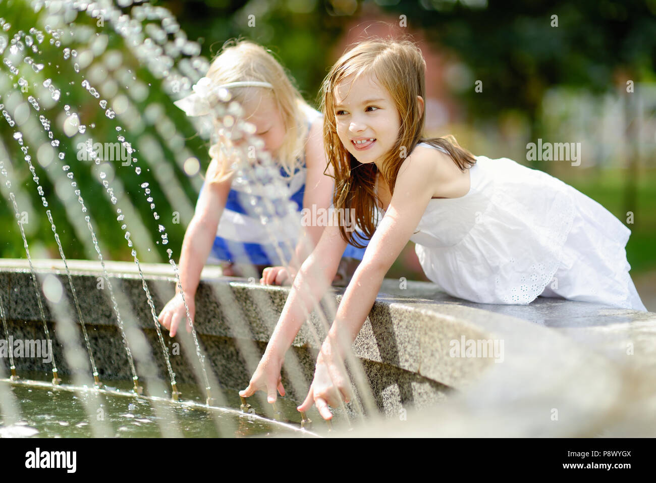 Two cute little girls playing with a city fountain on hot and sunny ...