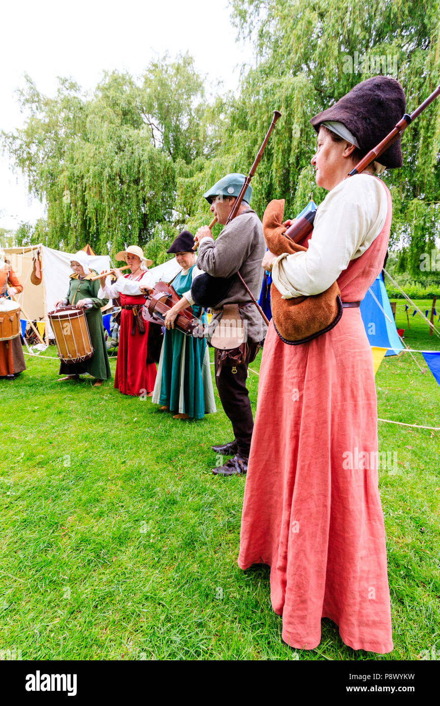 Medieval living history reenactment event. Band of traveling minstrels standing in line playing musical instruments outdoors. Bagpipes, drums, others. Stock Photo