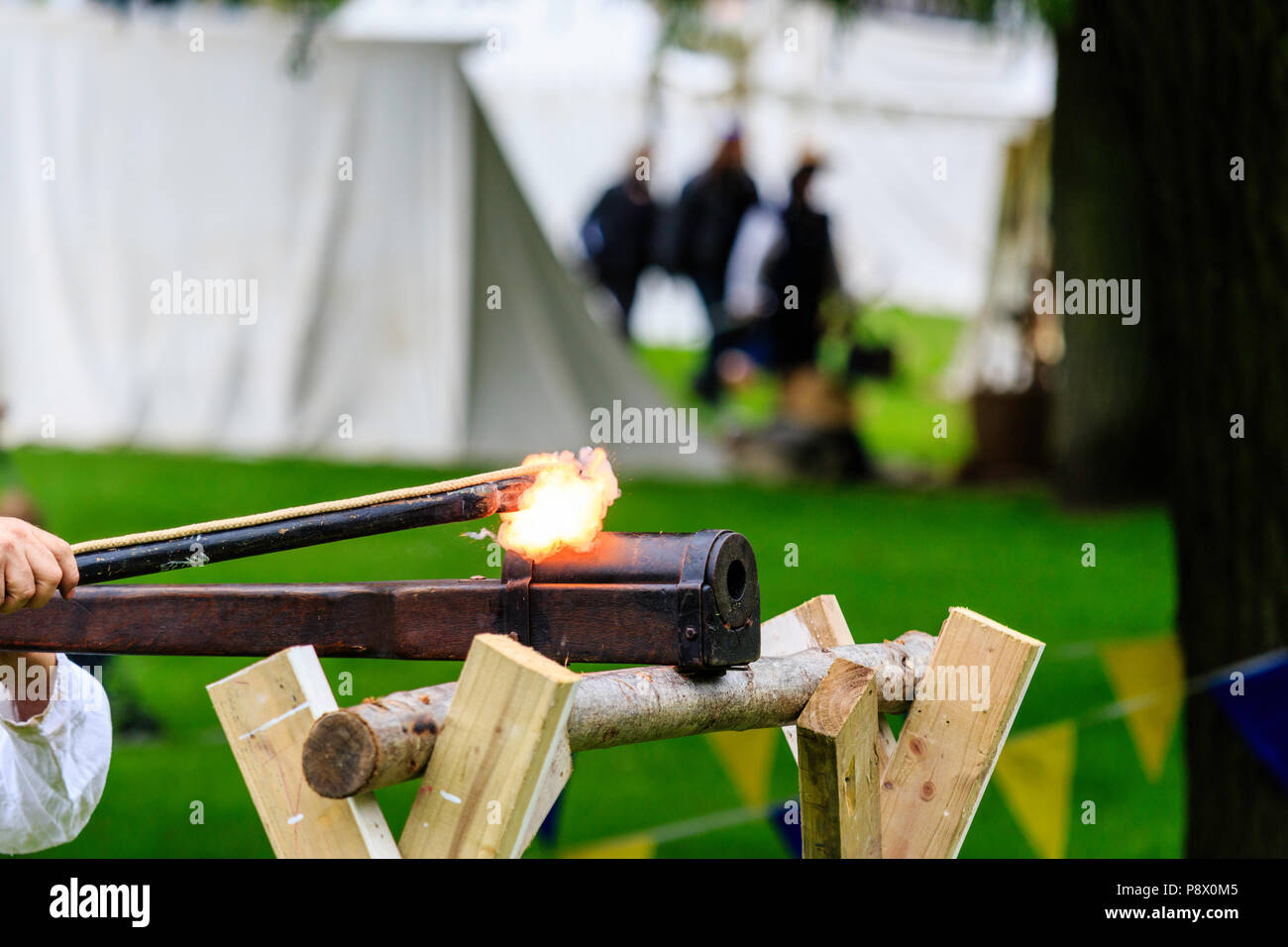 An early example of a German close-range hand cannon resting on wooden support with the fuse lit at medieval re-enactment event at Sandwich Stock Photo