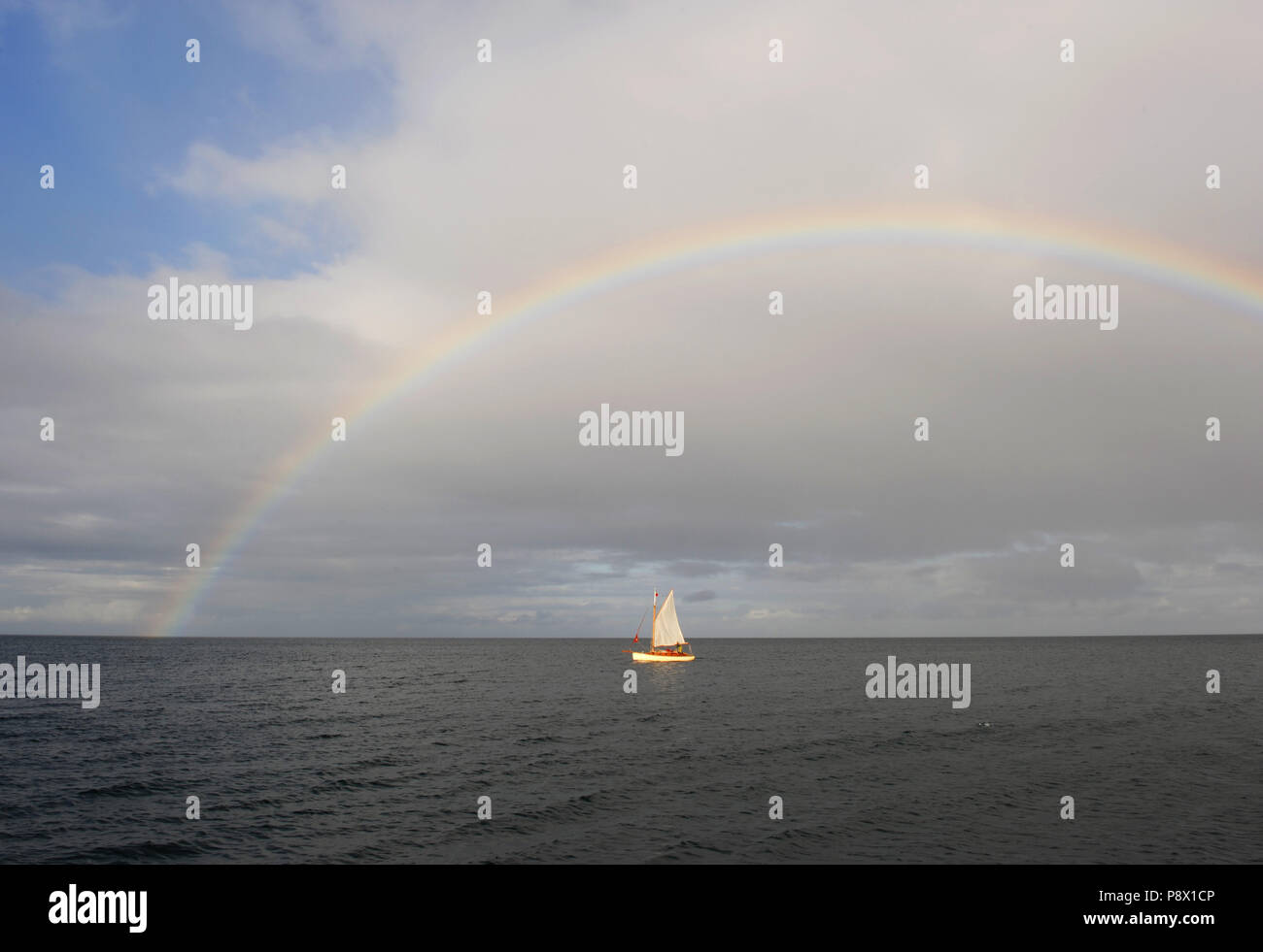 A small gaff rigged sailing boat sails beneath a huge rainbow in the Clyde Esturary, Scottand Stock Photo