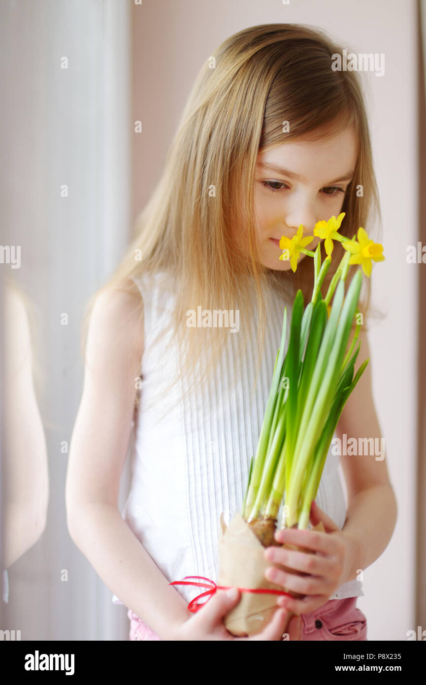 Adorable smiling little girl holding daffodils by the window Stock Photo