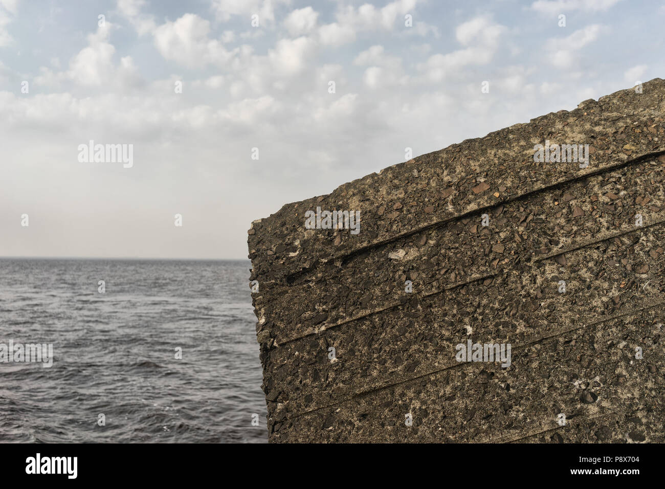 A fragment of a concrete wall with lines on the background of the sea waves and clouds on the horizon Stock Photo