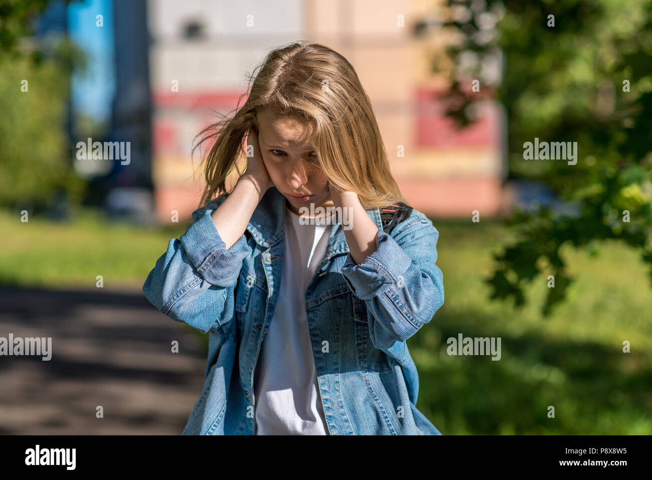 Teenage girl in summer outdoors. The palms of his hands close his ears. The concept of insult a misunderstanding, a loud noise. Emotions of discontent, bad behavior, sad and resentful child. Stock Photo