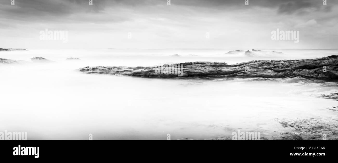 Calm ocean landscape time-lapse with smooth waves and rocks in black and white Stock Photo