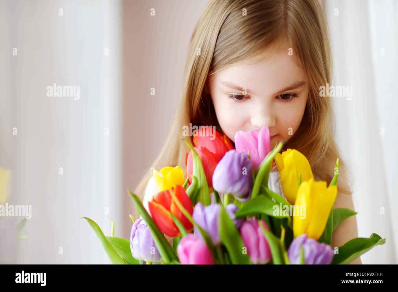 Adorable smiling little girl with tulips by the window Stock Photo - Alamy