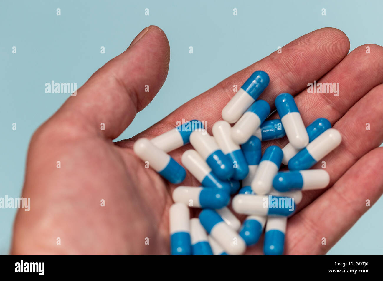 Hand holding drugs pills capsules on blue color background Stock Photo