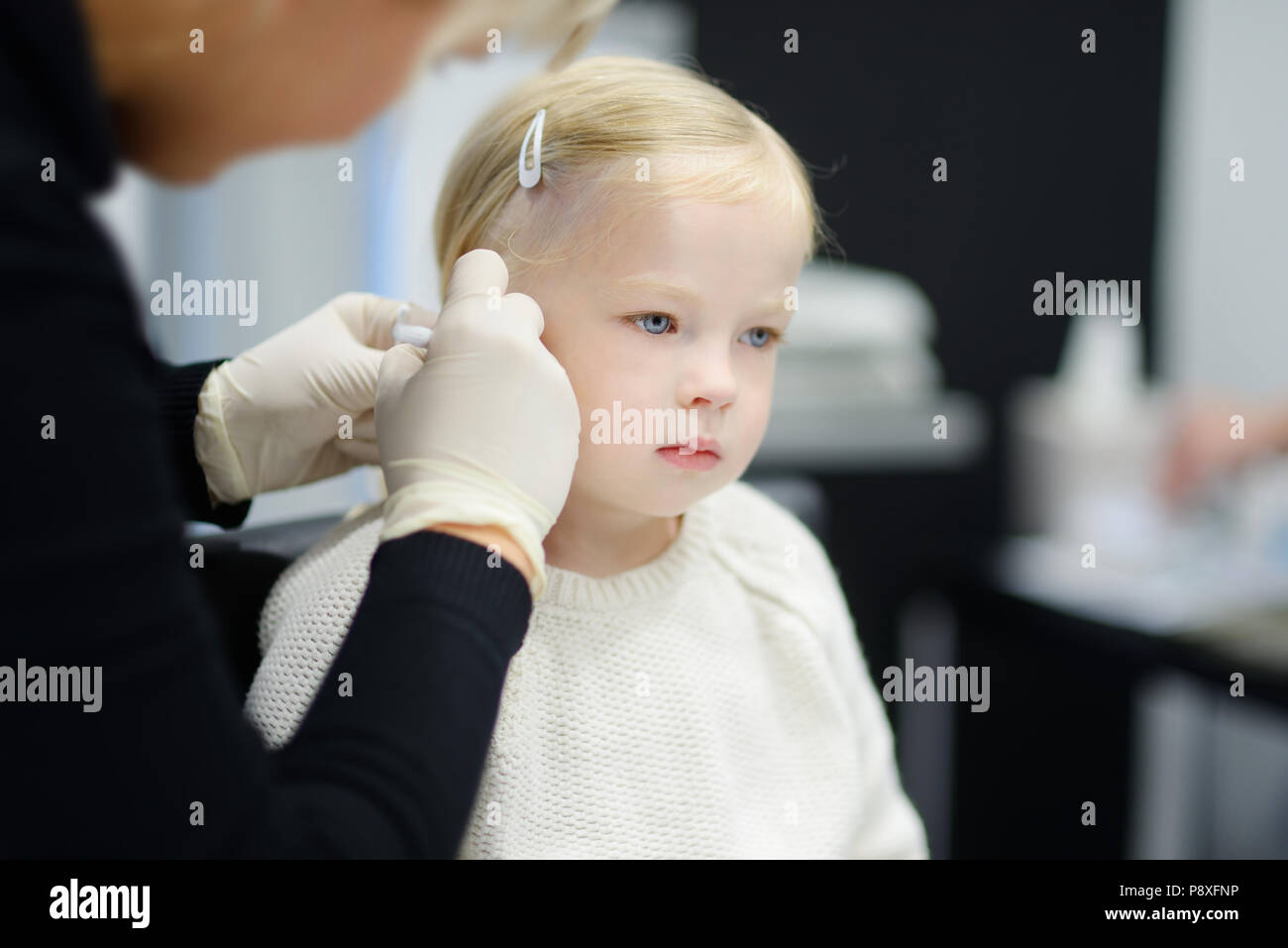 Adorable little girl having ear piercing process with special equipment in beauty center by