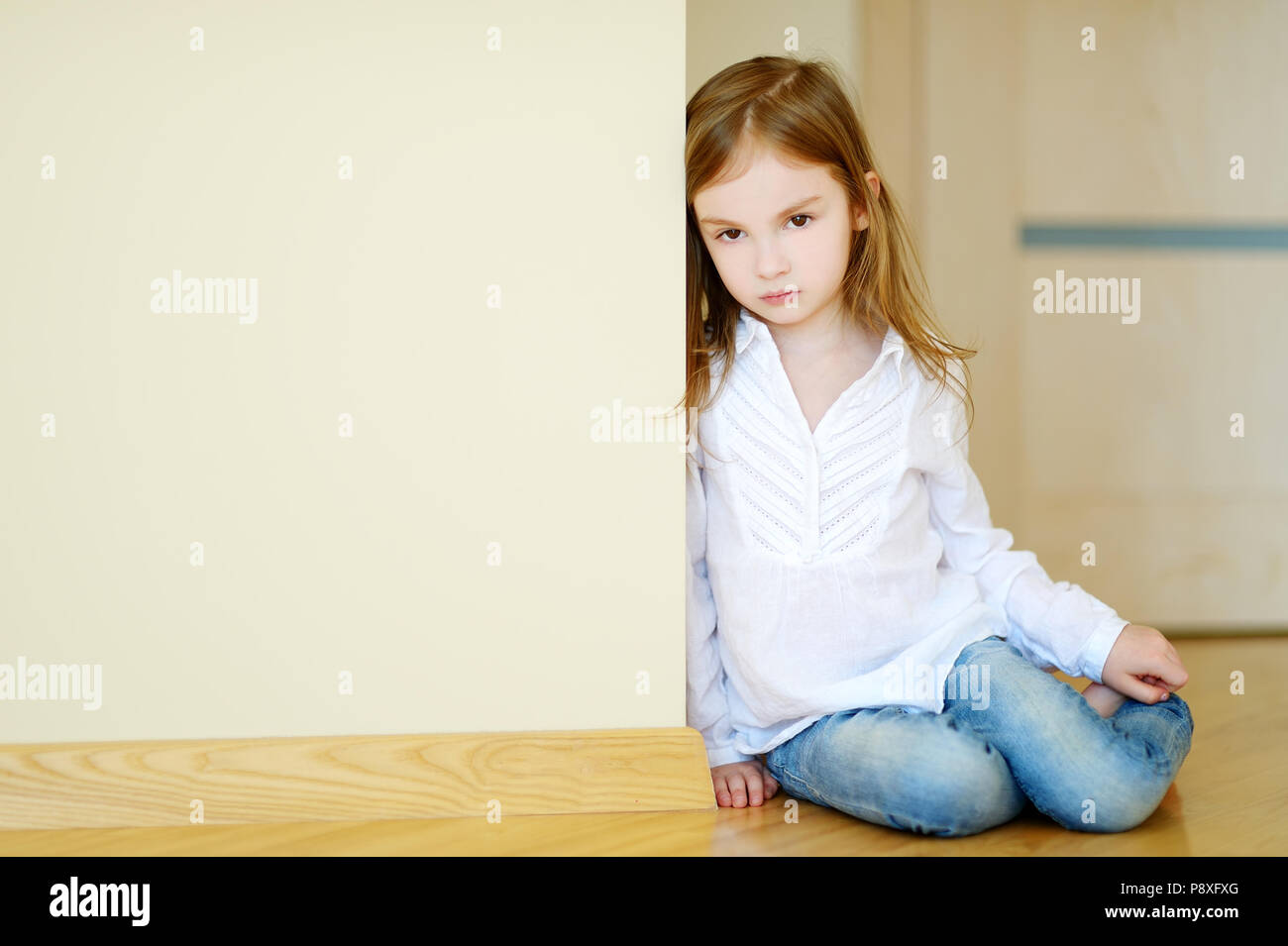 Sad little girl sitting on a floor at home Stock Photo - Alamy