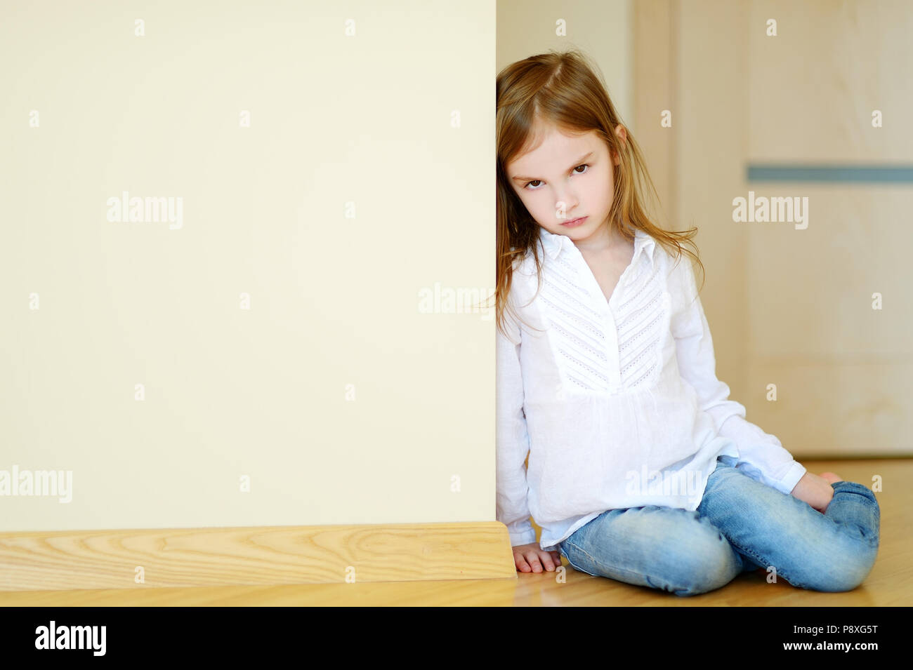 Sad little girl sitting on a floor at home Stock Photo - Alamy