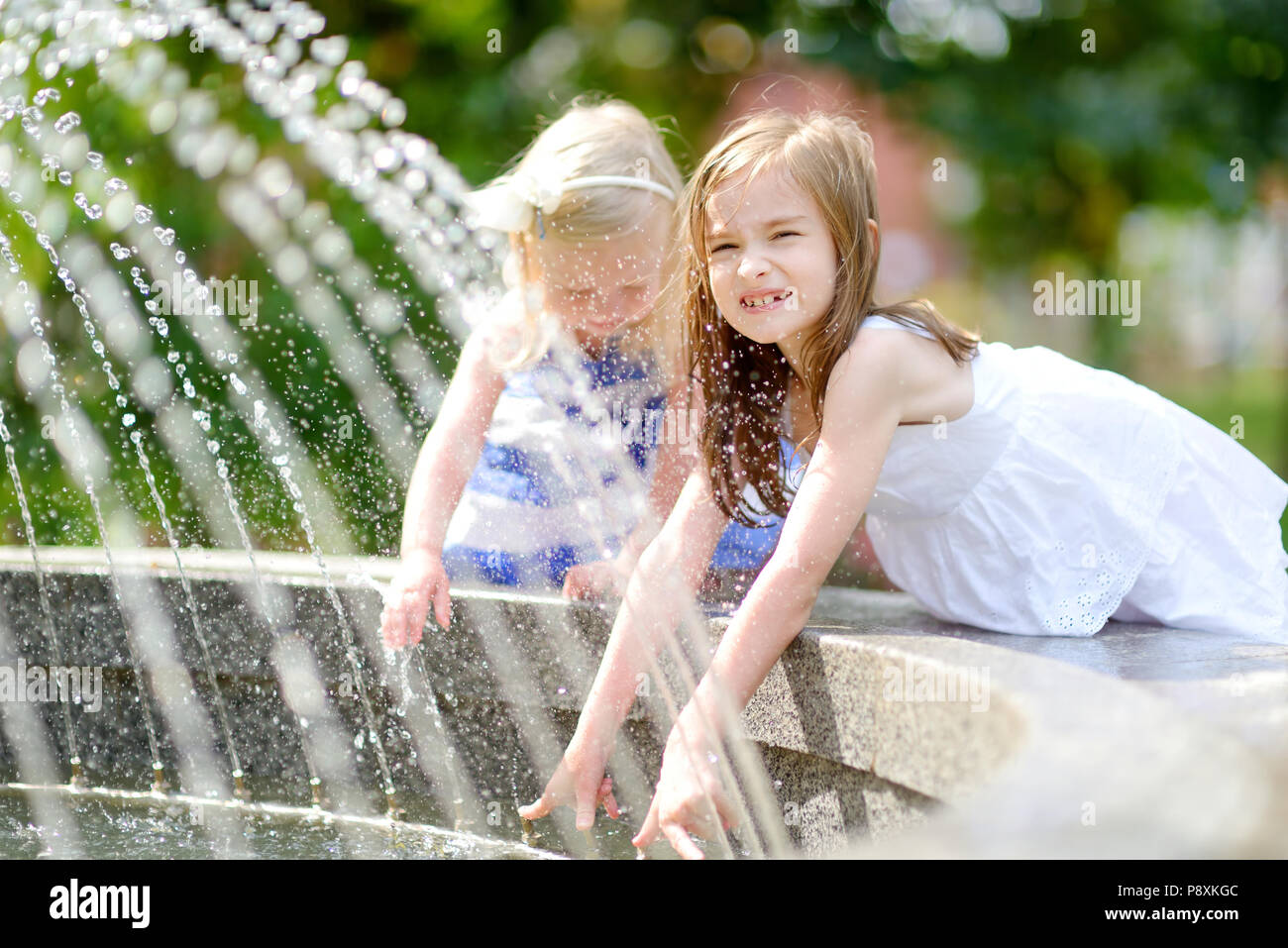 Two cute little girls playing with a city fountain on hot and sunny ...