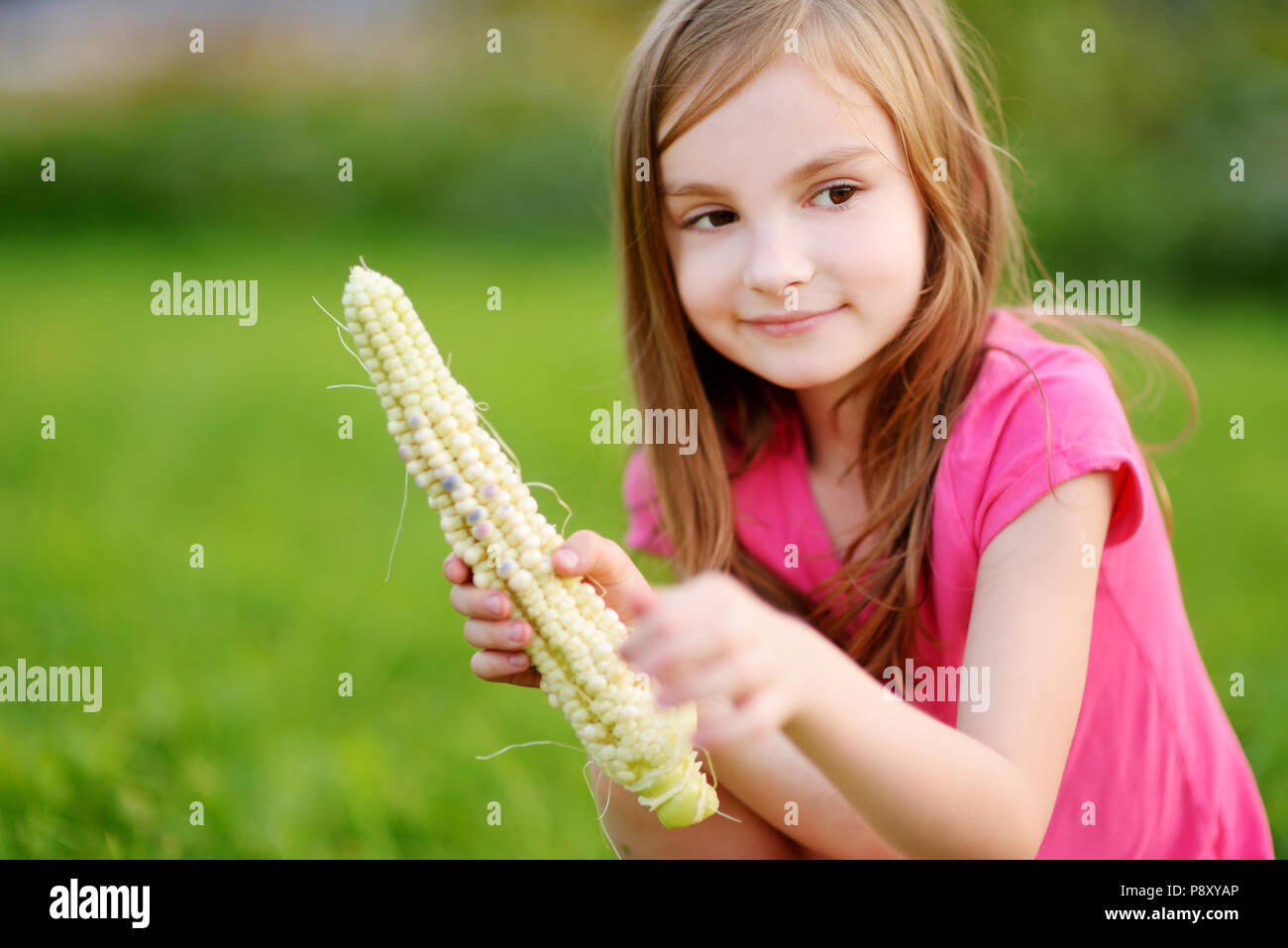 Pretty little girl holding a corn in the garden on beautiful autumn day