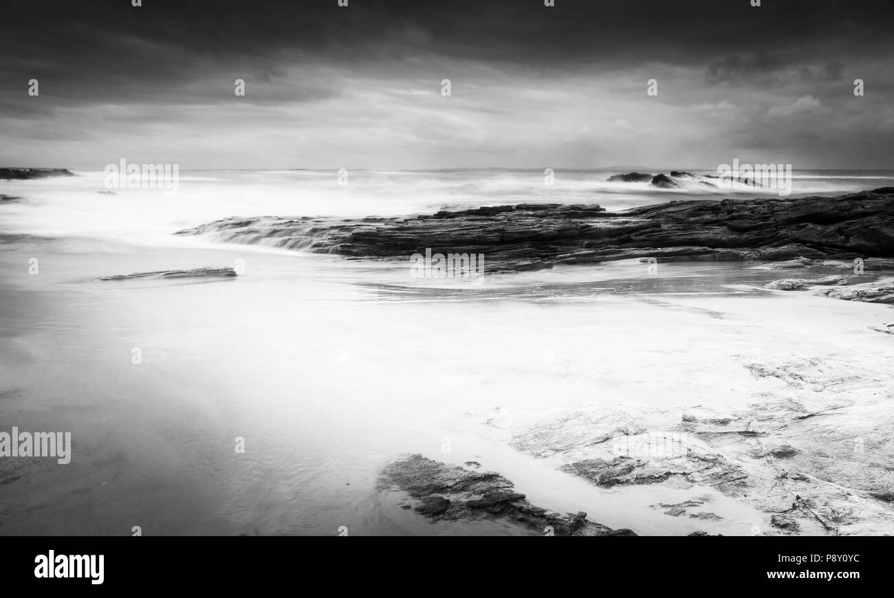 Stormy beach landscape time-lapse with smooth waves and rocks in black and white Stock Photo