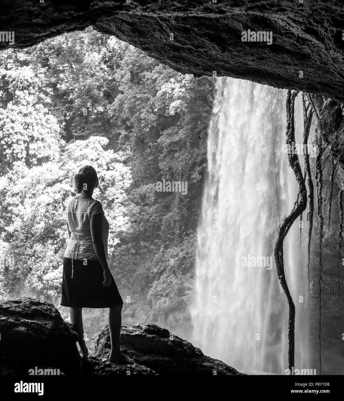 Tourist In cave looking out at Misol Ha Waterfall near Palenque in Chiapas, Mexico in black and white Stock Photo
