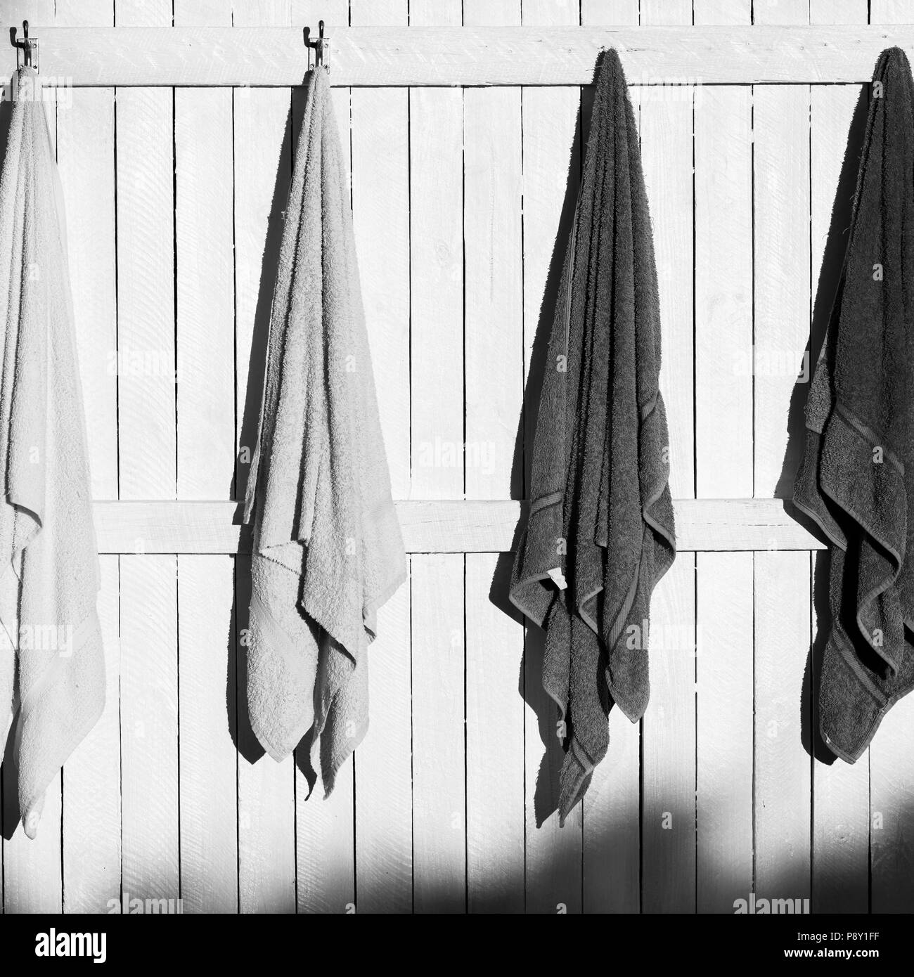 Towels hanging outdoors on hooks in the sun in black and white Stock Photo