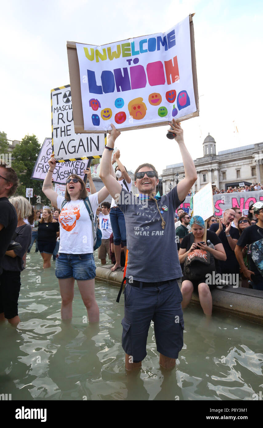 Demonstrators holding placards stand in the fountains in Trafalgar Square, London, as they take part in protests against the visit of US President Donald Trump to the UK. Stock Photo
