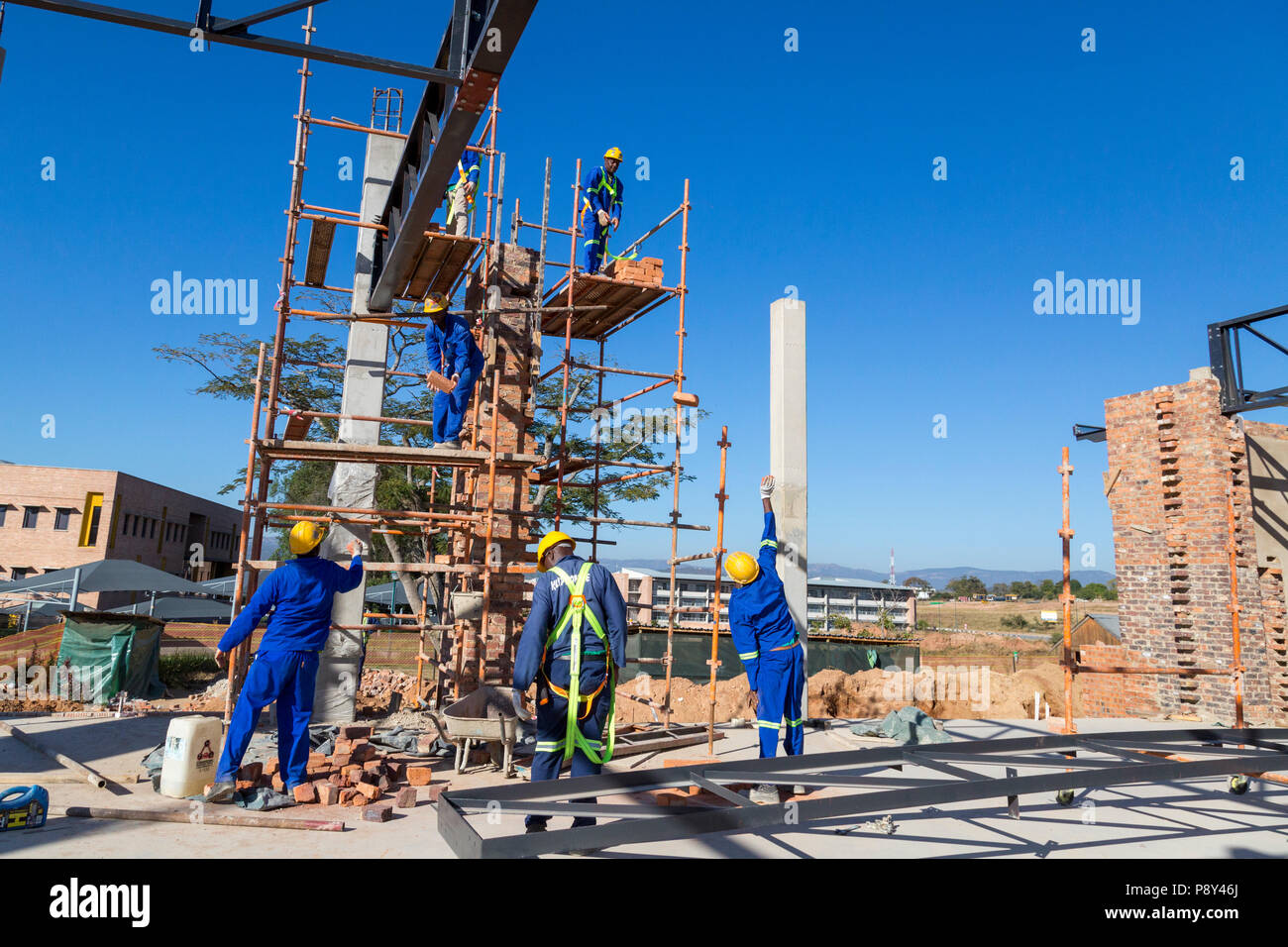 Brick layers passing bricks up to workers on a scaffolding in preparation for brick laying Stock Photo