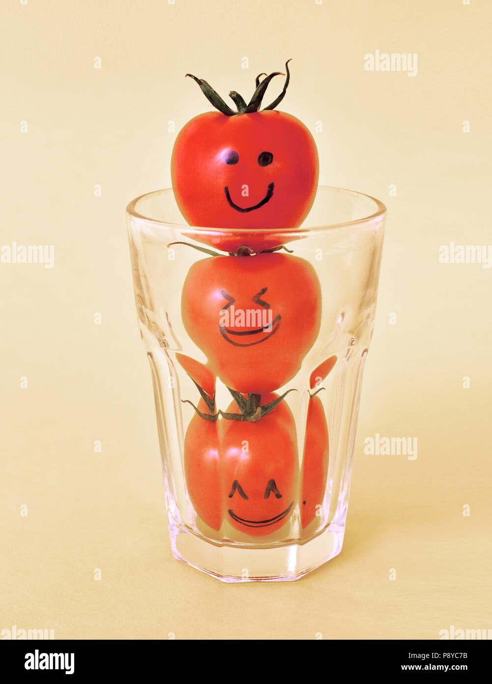 Three tomatoes with eyes and mouths drawn in black ink in a glass. Stock Photo