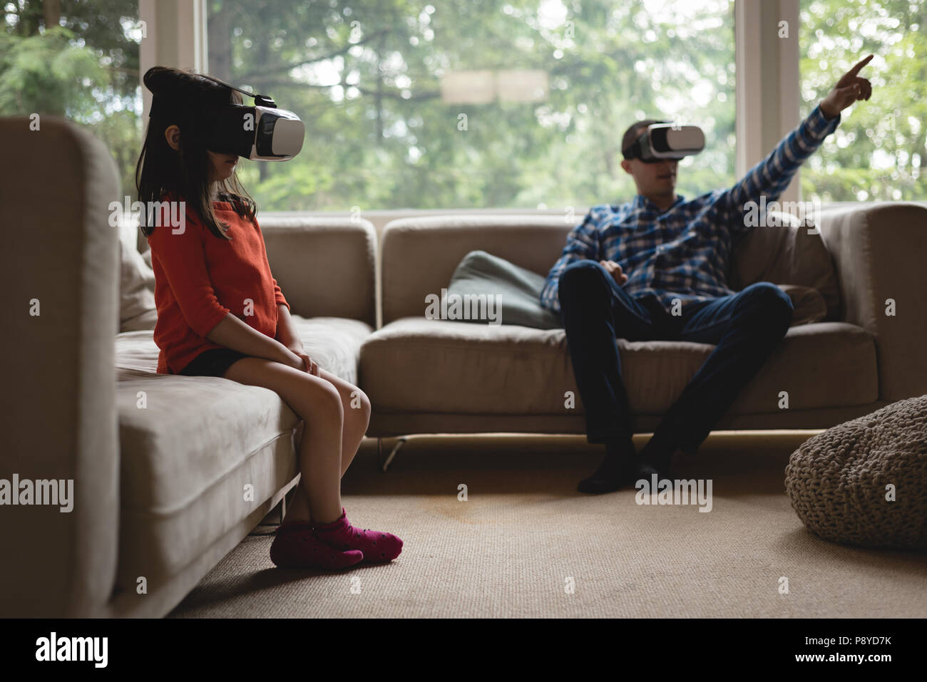 Father and daughter using virtual reality headset in living room Stock Photo