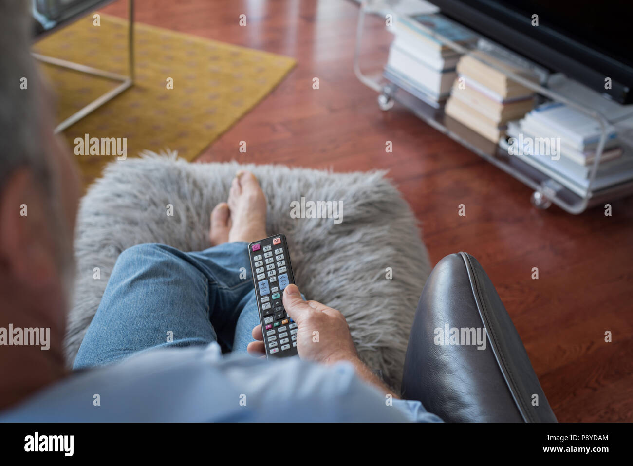 Man changing channels while watching television in living room Stock Photo