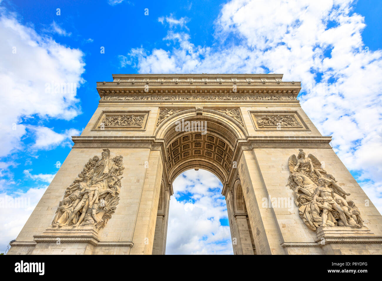 Bottom view of Arch of Triumph at center of Place Charles de Gaulle with clouds and blue sky. Popular landmark and famous tourist attraction in Paris capital of France in Europe. Stock Photo