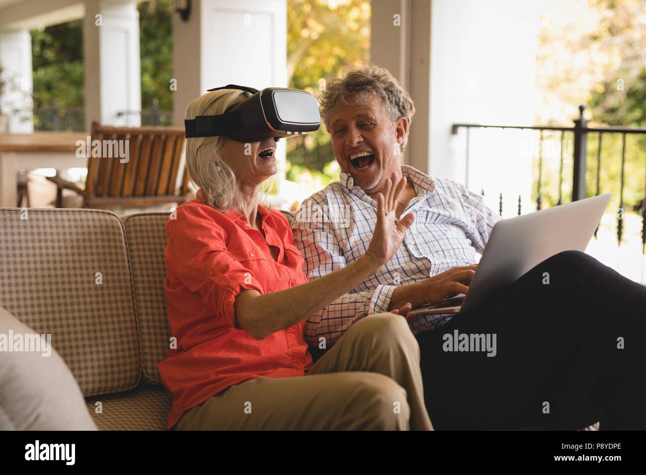 Senior couple using laptop and experiencing VR headset in porch Stock Photo