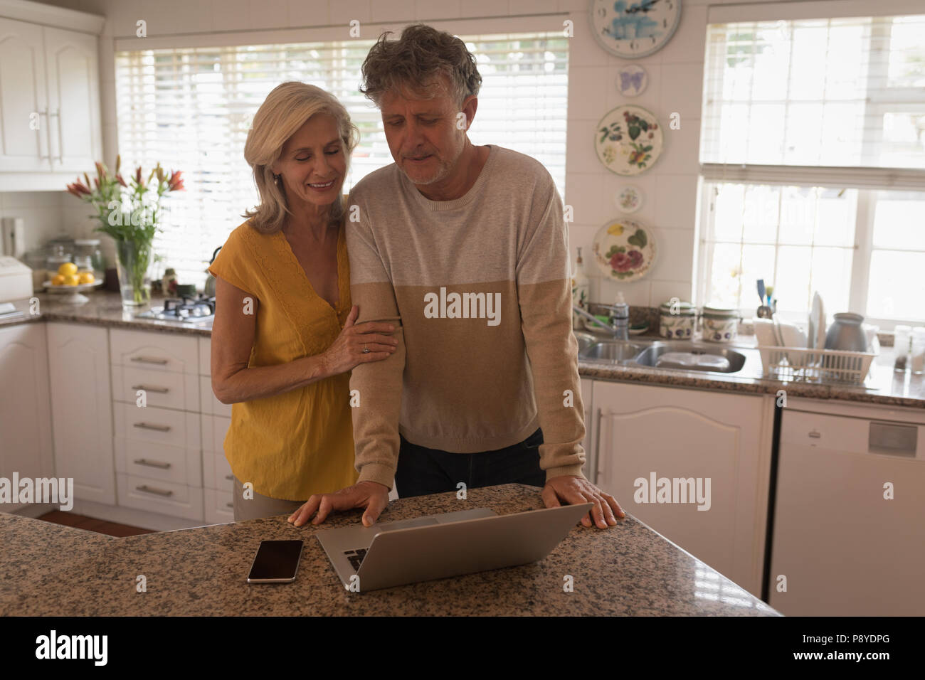 Smiling senior couple using laptop in the kitchen Stock Photo