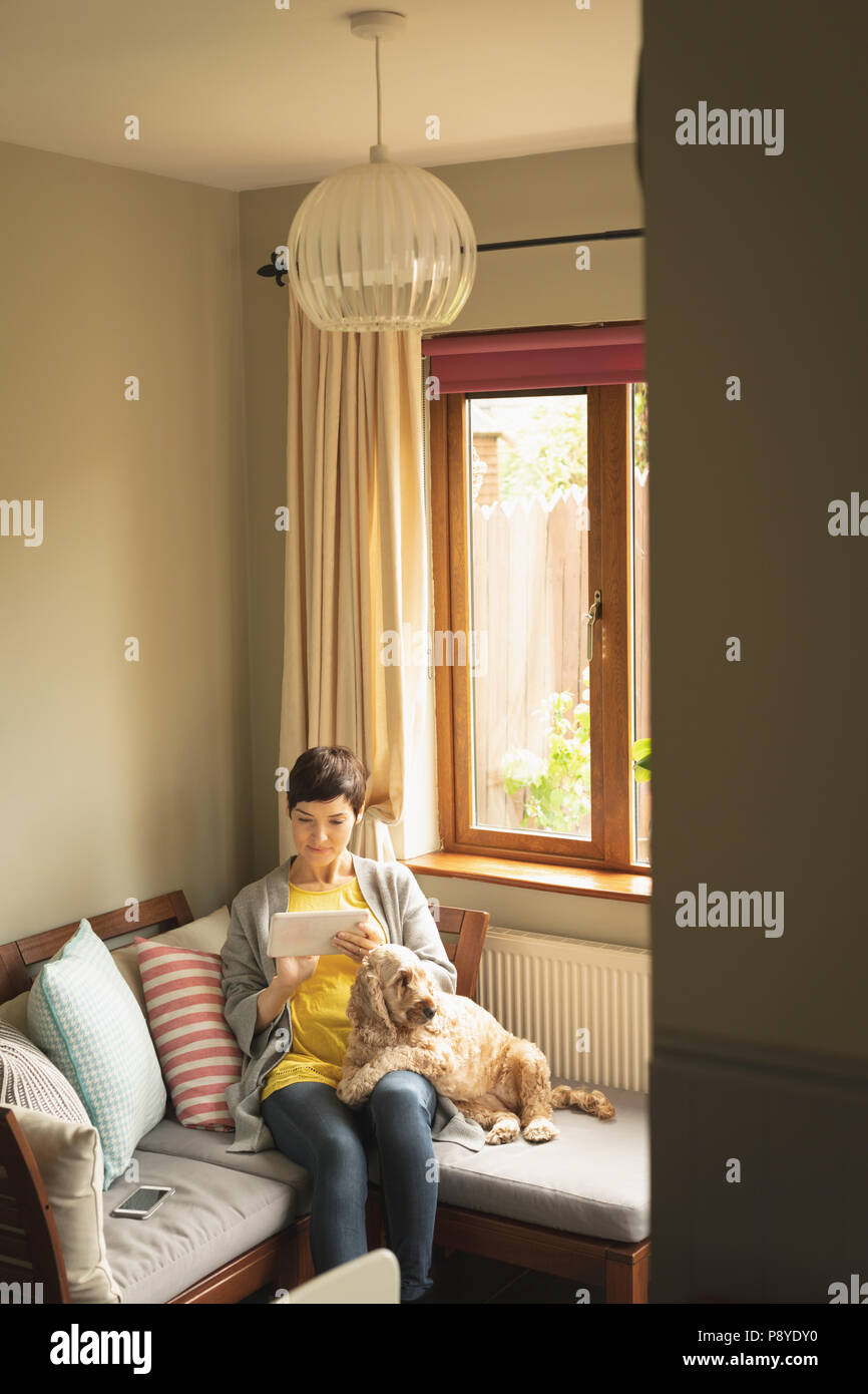 Woman using digital tablet with dog on sofa in living room Stock Photo