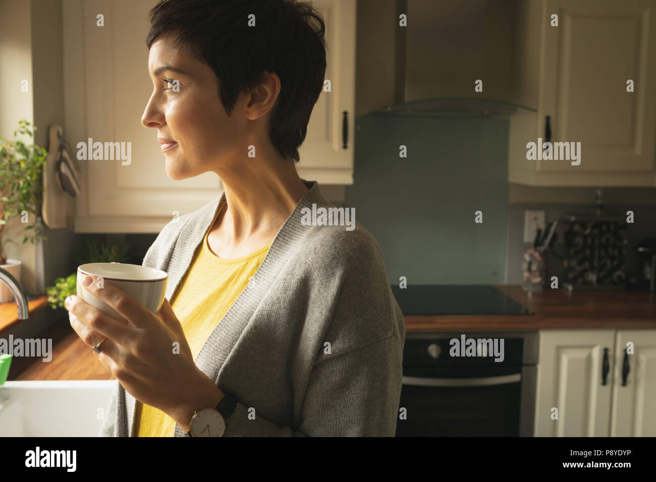 Woman looking away while having coffee in the kitchen Stock Photo