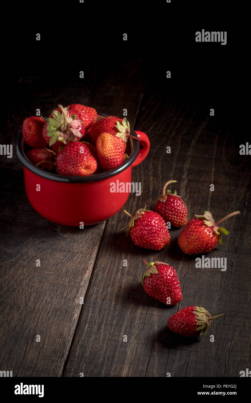 Strawberries in an iron mug on a wooden table. Dark photo of a ...