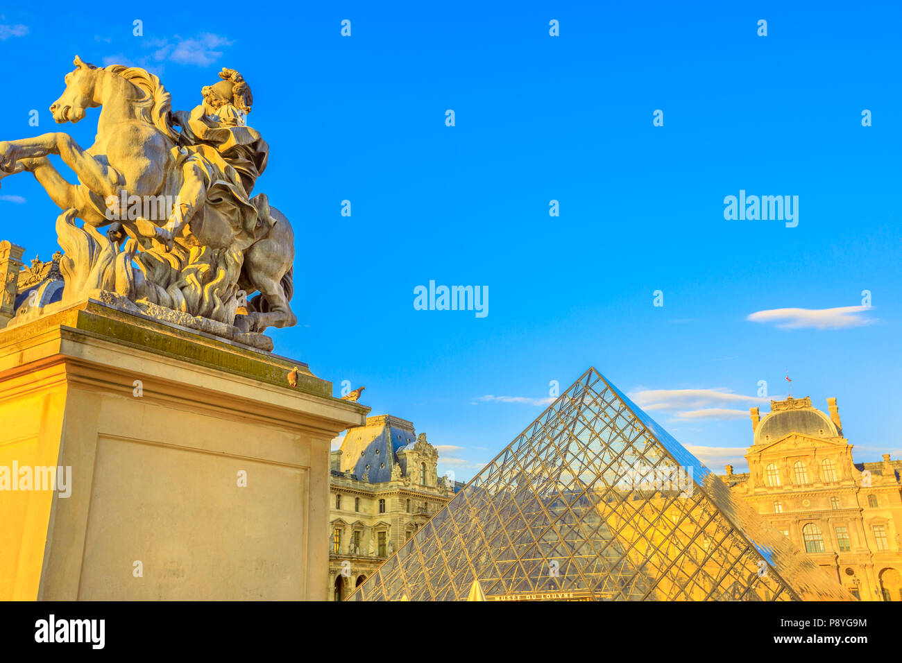 Paris, France - July 1, 2017: King Louis XIV Equestrian Statue At Musee Du Louvre on foreground. Glass Pyramid and Pavillon Rishelieu on the background. Louvre Palace is a famous landmark of Paris Stock Photo