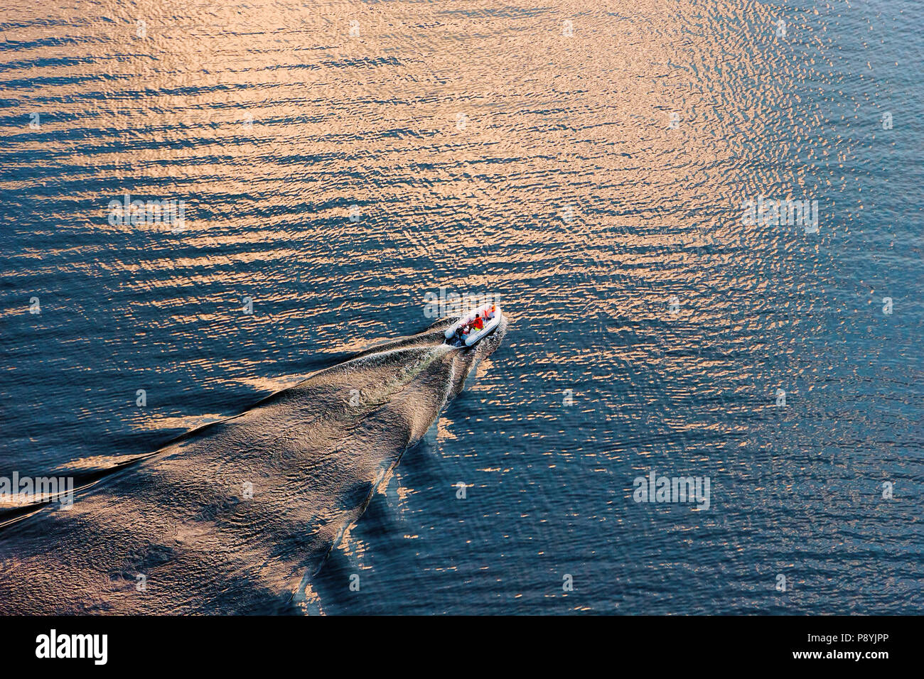 Aerial view of a small boat on wide blue water surface in evening sun. Diagonal composition suitable background. Stock Photo