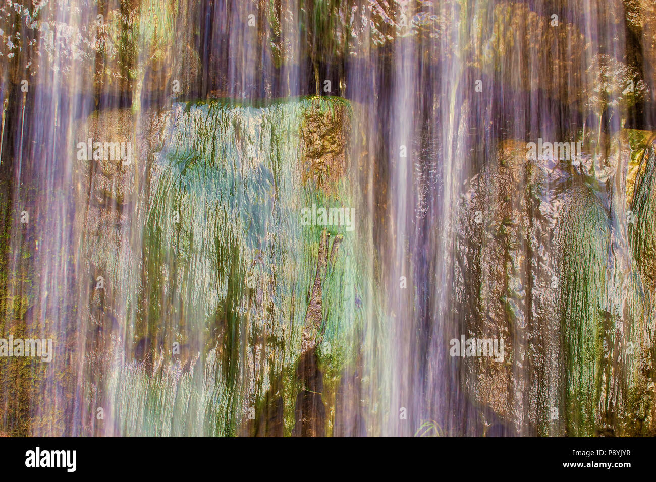 Abstract background image of waterfall flowing over green rocks, close-up. Stock Photo