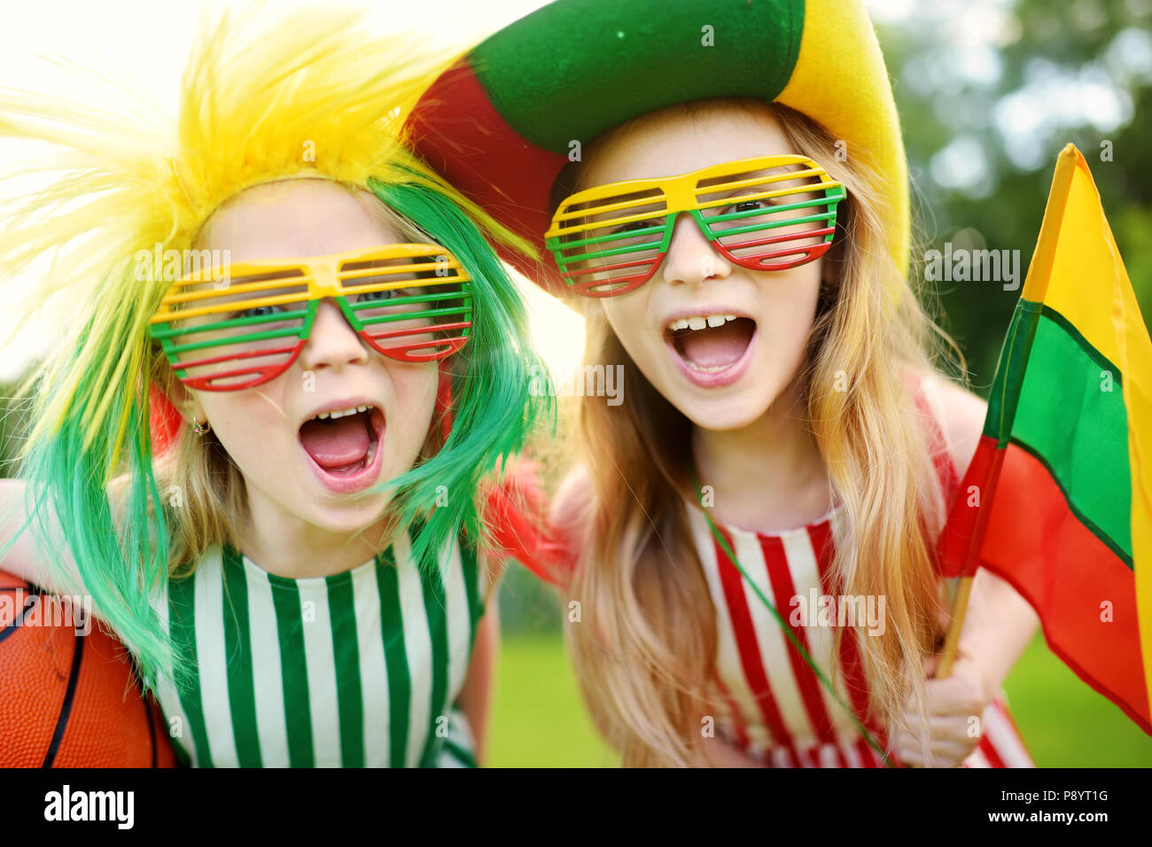 Two funny little sisters supporting and cheering their national basketball team during basketball championship. Two cute Lithuanian team fans. Stock Photo