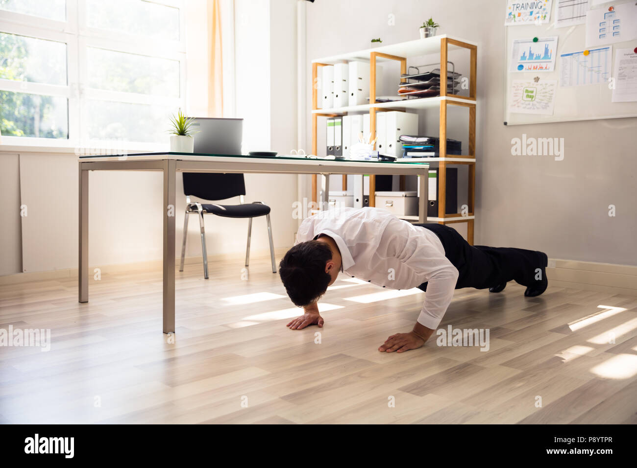 Businessman doing push up on hardwood floor in office Stock Photo