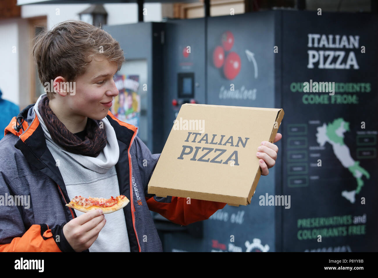 Reischach, Italy, boy proudly shows the box of his pizza pulled out of a machine Stock Photo
