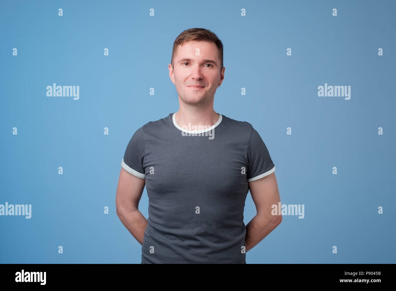 Confident young handsome man keeping arms crossed and smiling while standing against blue white background Stock Photo